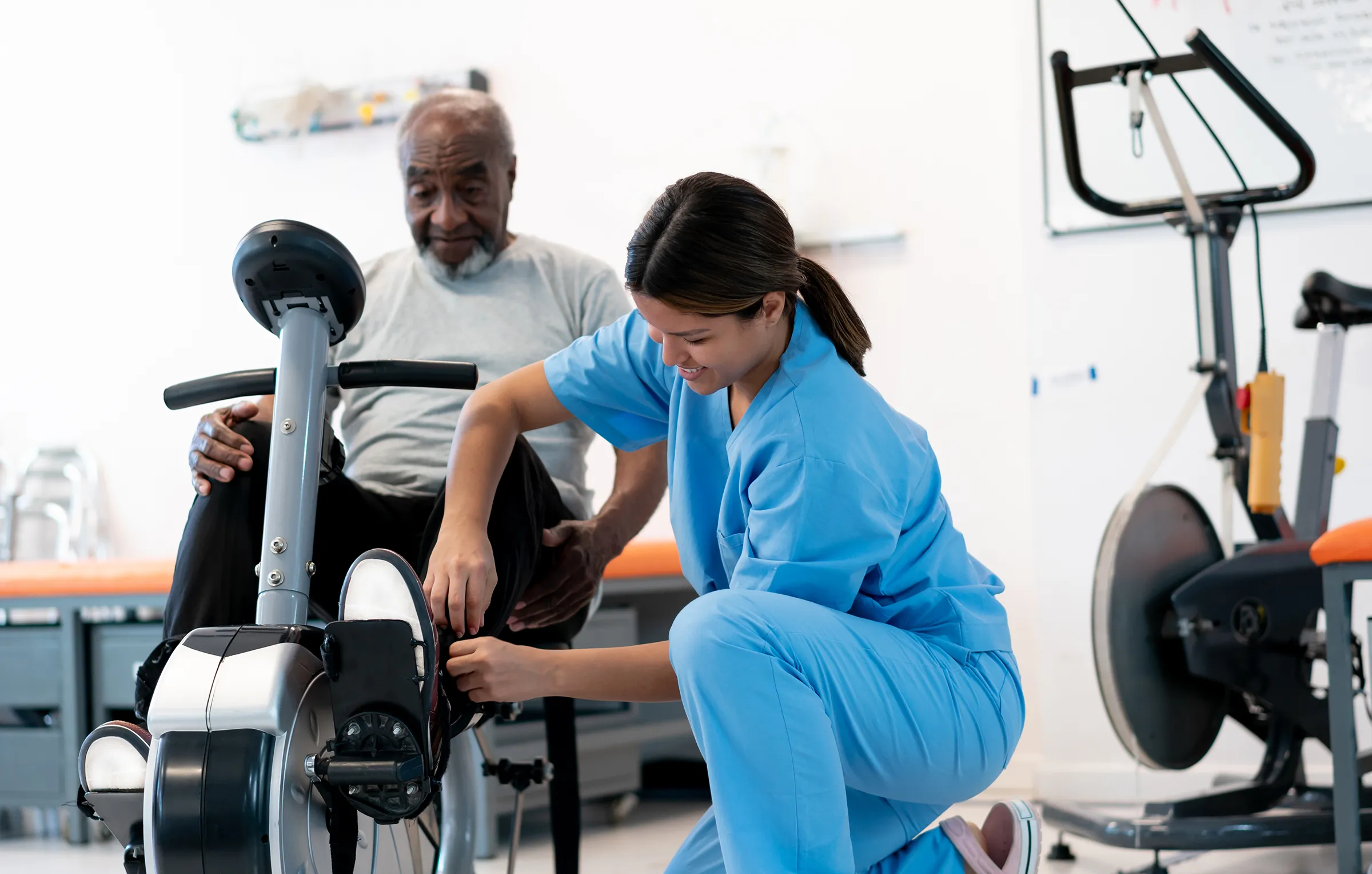 Physical therapist assisting senior on exercise bike