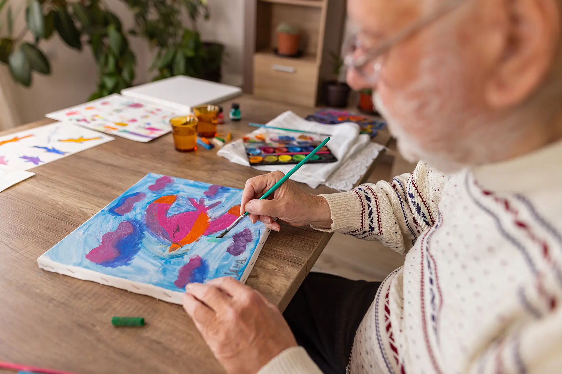 Elderly man painting colorful bird on canvas