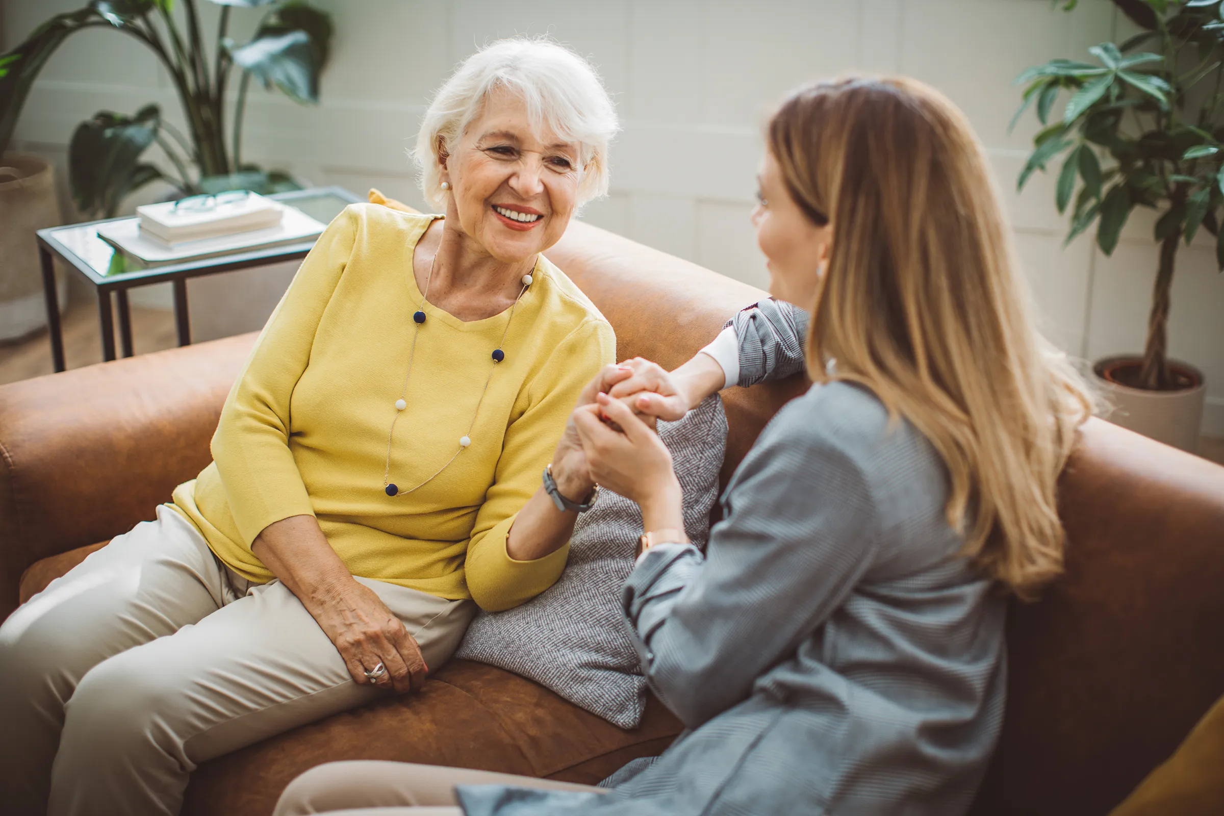 Elderly woman holding hands with caregiver on couch