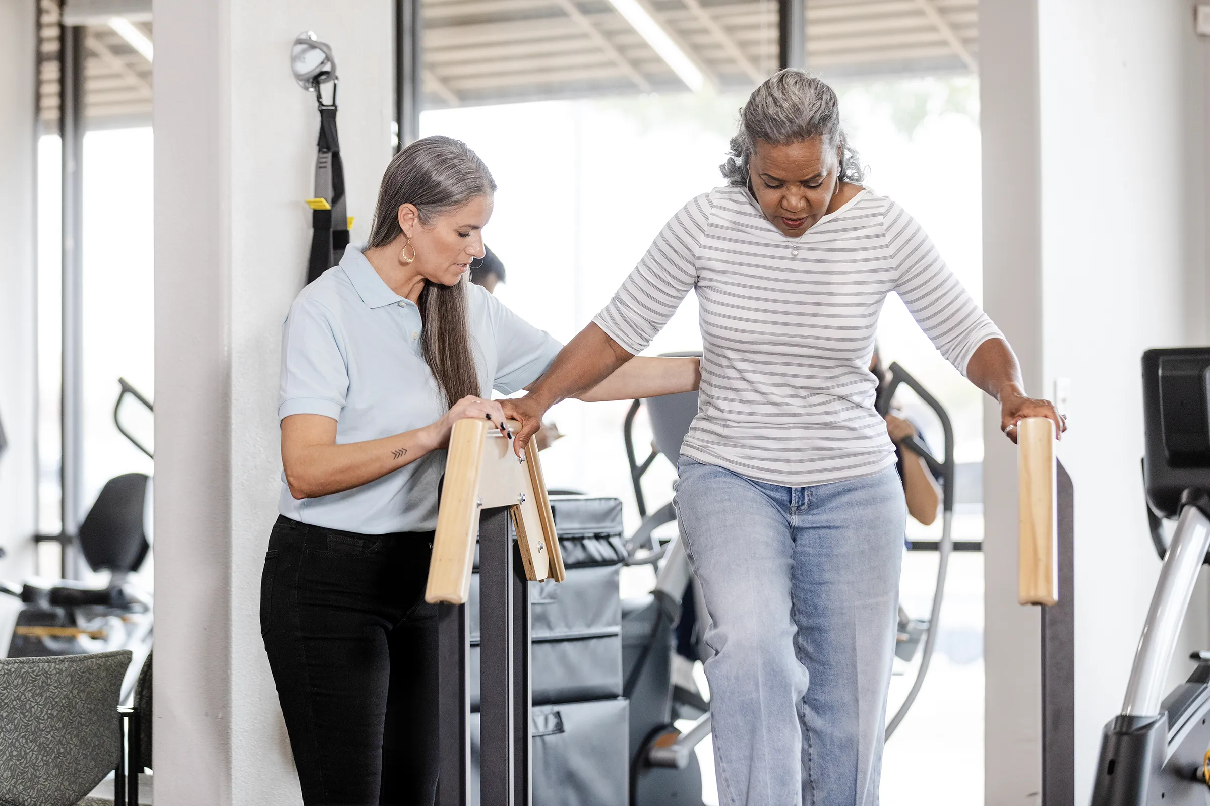 Physical therapist assisting woman with parallel bars